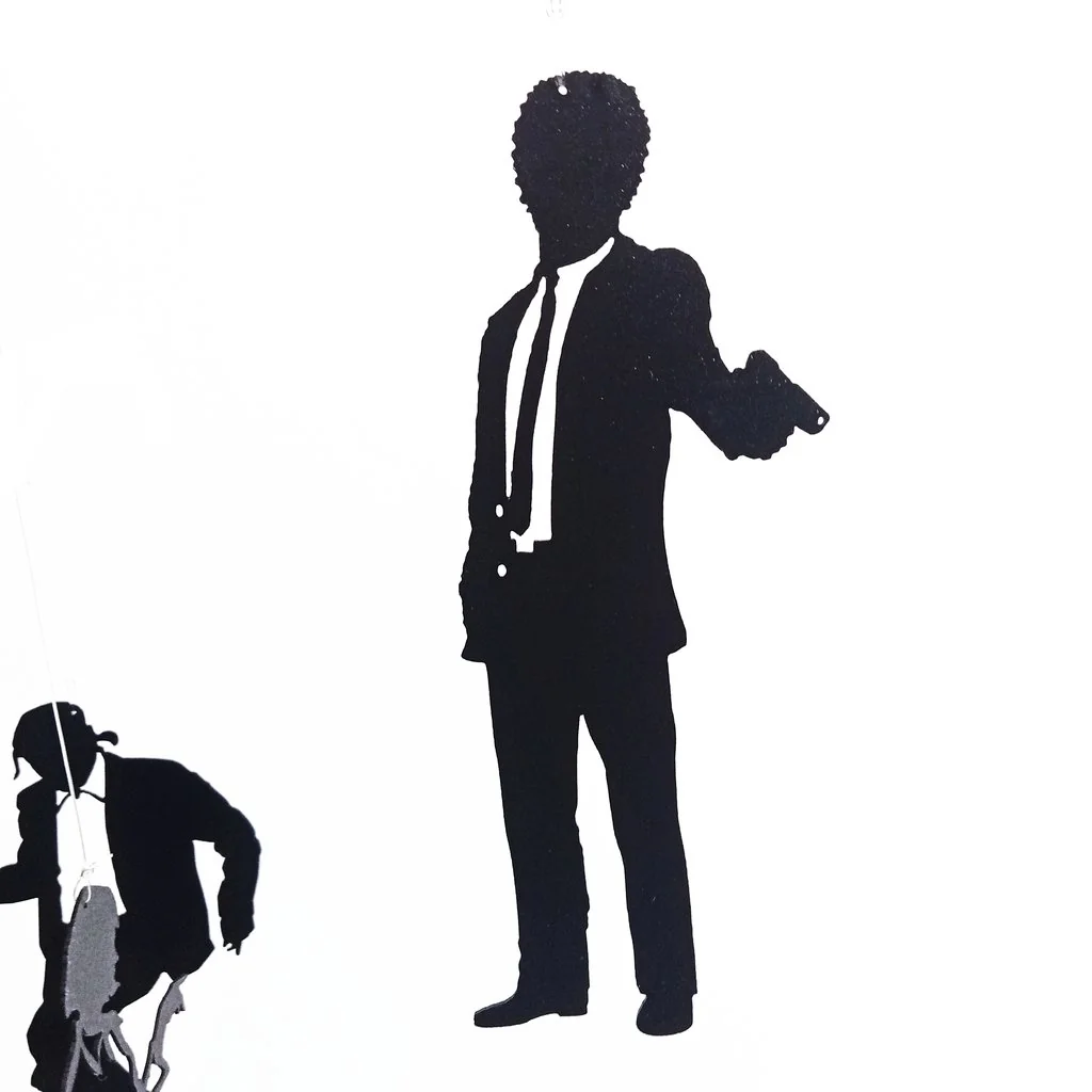 Silueta negra de Jules Winnfield con traje y pistola en mano, detalle del móvil decorativo de Pulp Fiction.