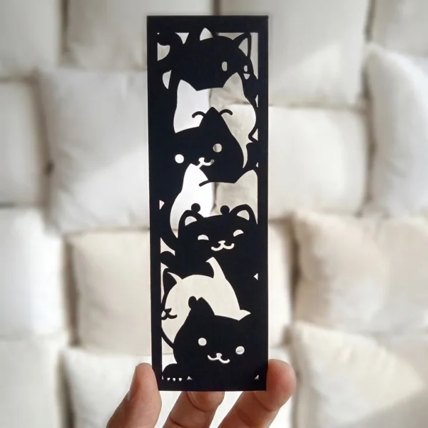 Marcapáginas troquelado de Gatos Kawaii en negro mate con fondo de almohadones blancos, diseño resistente en polipropileno
